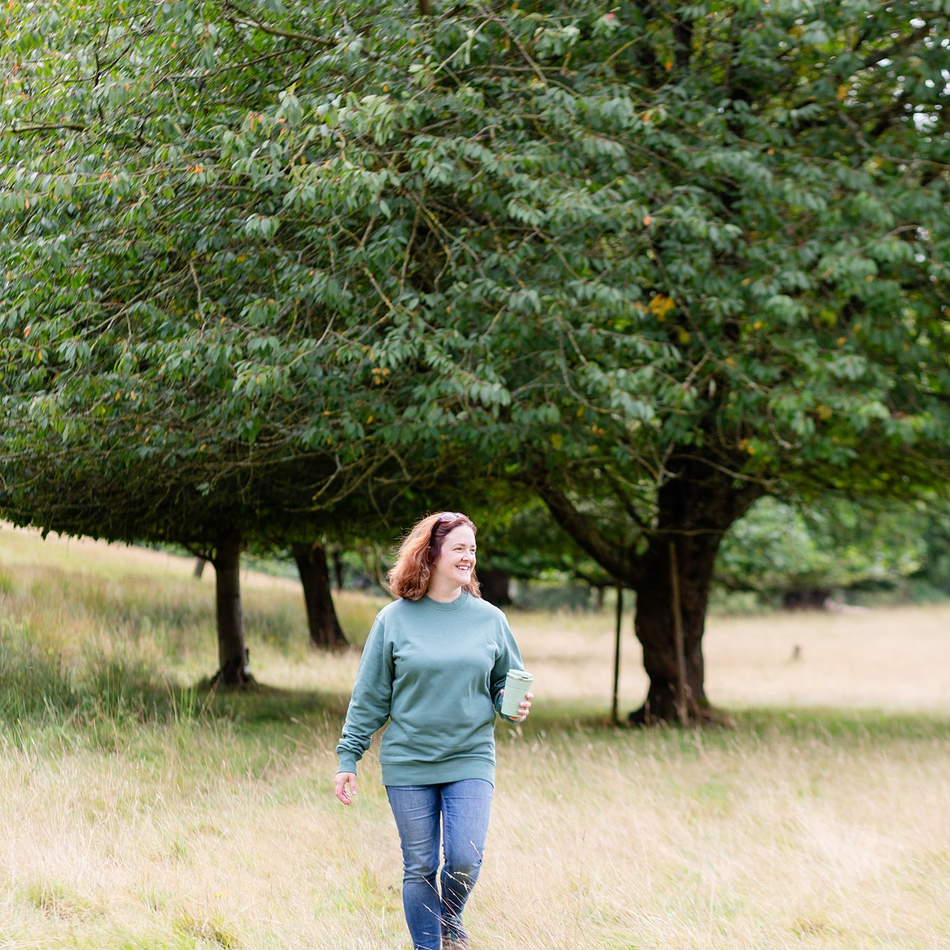 Person wearing a Hue & Harmony sweatshirt in Green Bay, walking through a field. Trees in background.