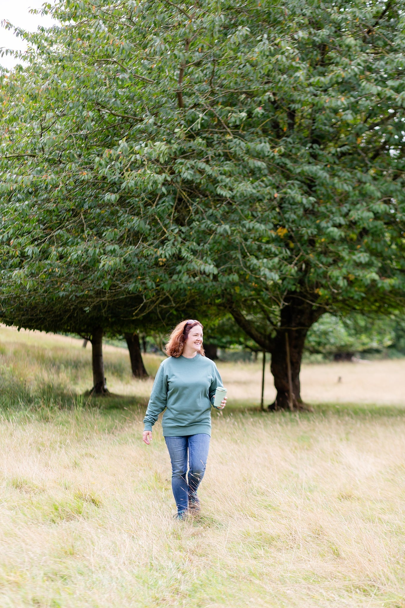 Person wearing a Hue & Harmony sweatshirt in Green Bay, walking through a field. Trees in background.